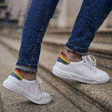 Weißer Pride Sneaker mit Regenbogen Farben an der Fersenkappe von BGENTS am Fuß auf Treppen